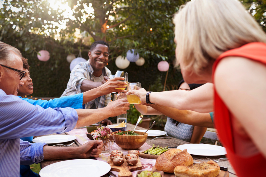 Friends toast with glasses over a table of food during an outdoor garden party decorated with paper lanterns.